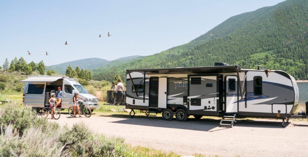 large travel trailer in mountains with family on bikes outside it