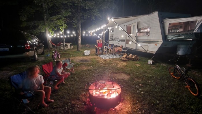 family sitting outside RV at night with campfire and led lights