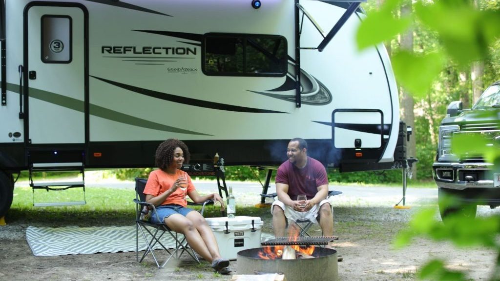 couple sitting at camp fire outside their Grand Design Reflection travel trailer