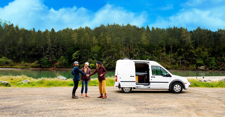 3 people, 2 shaking hands, outside in front of van RV