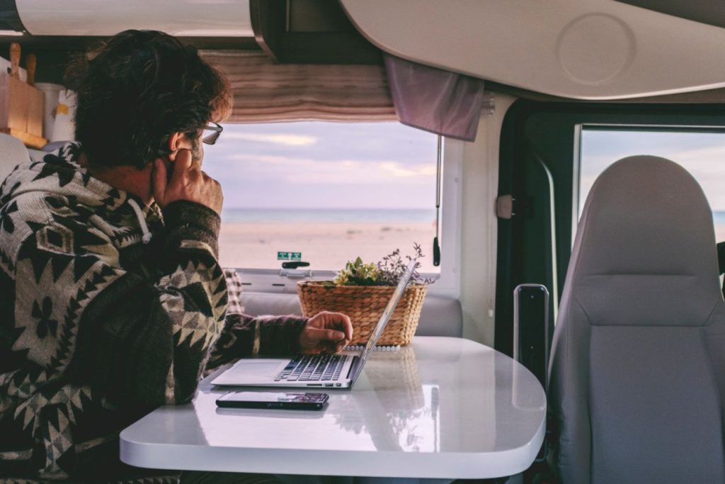 Man looking out window of RV while working on laptop