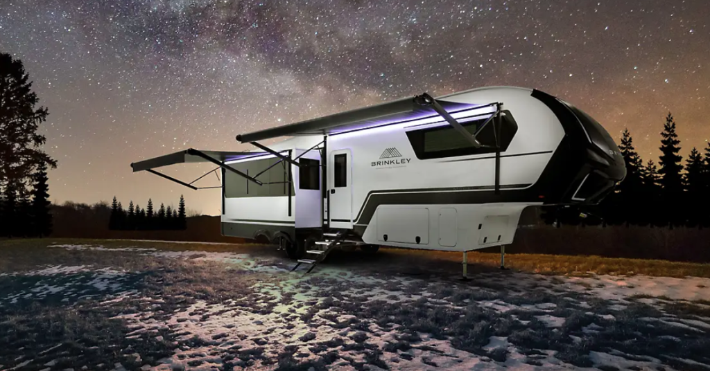 Brinkley Model Z 2680 fifth wheel parked outdoors under a star-filled night sky, with its slide-out awnings extended and illuminated LED accents highlighting the sleek design.