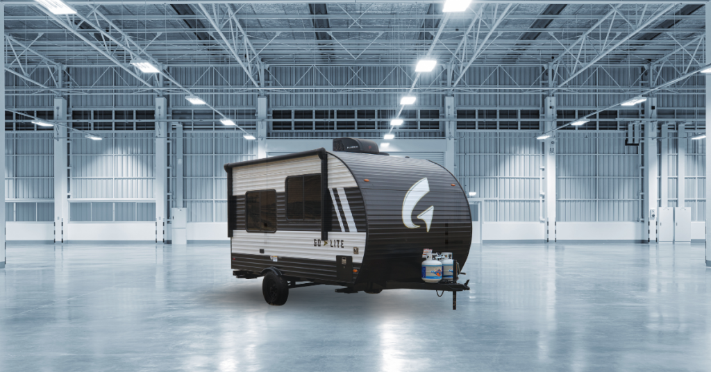 Go  Lite travel trailer displayed in a spacious, well-lit industrial showroom. The trailer features a sleek black and white exterior with aerodynamic design, showcasing its compact and lightweight build. The empty, modern facility highlights the trailer’s stylish appearance and durability