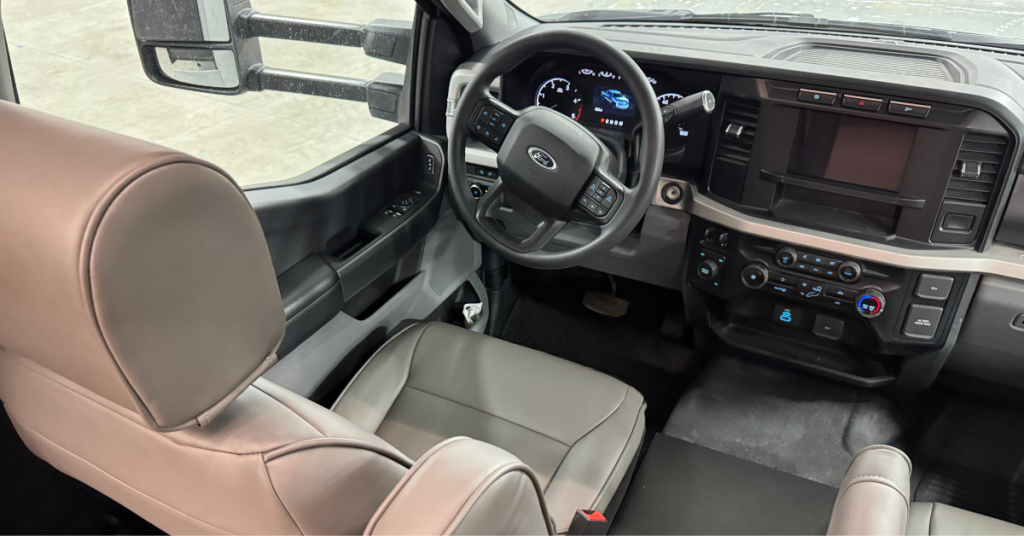 Driver's cockpit of a motorhome featuring a modern and ergonomic design. The dashboard includes a steering wheel with integrated controls, a digital instrument cluster, and a large central display screen for navigation and infotainment. The leather seating provides comfort, while large side mirrors with extendable arms enhance visibility for safe driving. The layout emphasizes functionality and driver convenience.