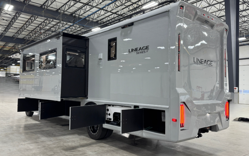 Rear and side view of a motorhome with a sleek white exterior, branded as 'Lineage Series F.' The motorhome features extended storage compartments with open doors, a slide-out section for increased interior space, and integrated rear lighting. The design emphasizes both functionality and modern aesthetics, with the vehicle parked in a large indoor facility.