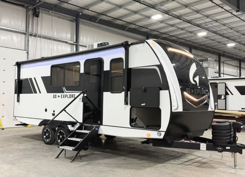 This image showcases an RV from the "Go Explore" series. It features a sleek, modern design with clean black-and-white styling and bold graphics. The dual-axle system ensures stability, while the entry steps appear sturdy and foldable for convenience. The large windows and aerodynamic front cap with illuminated accents enhance both functionality and aesthetics. This model appears well-suited for adventurous families or individuals seeking comfort and utility in a travel trailer.