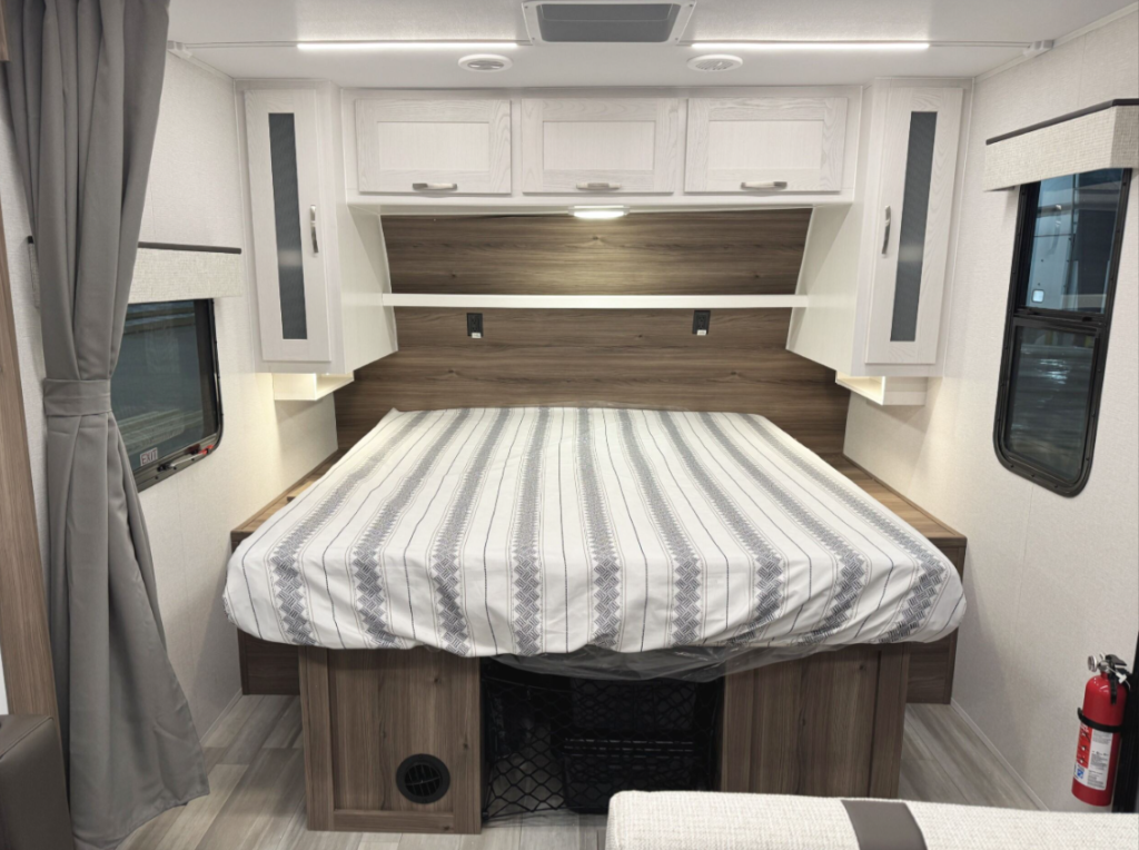 This RV bedroom features a clean and functional design, with overhead cabinets, side wardrobes, and ambient lighting to create a comfortable and organized sleeping space. The centered queen bed adds to the room's spaciousness and practicality. 