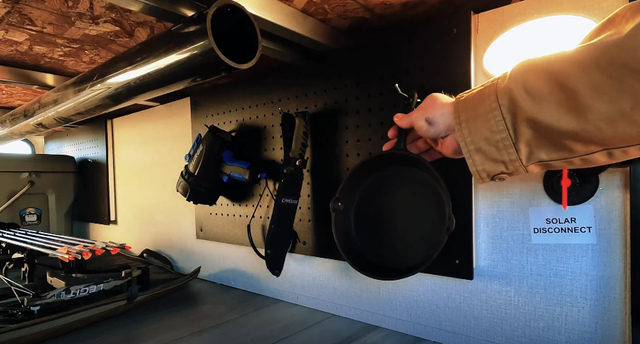 This image displays an organized storage area with a pegboard system, allowing tools and equipment like a cast-iron pan, knife, and other items to be securely mounted and accessible. The addition of a solar disconnect switch highlights functionality for managing the RV’s solar power system. This setup is ideal for RV owners who prioritize practical organization and ease of use in their storage compartments